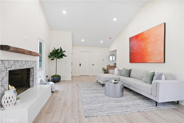living room with high vaulted ceiling, a tile fireplace, light wood-style flooring, baseboards, and recessed lighting