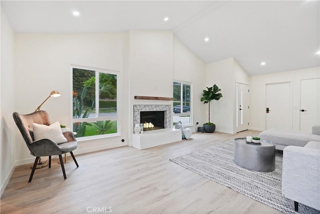 living area featuring a fireplace, baseboards, light wood finished floors, and high vaulted ceiling