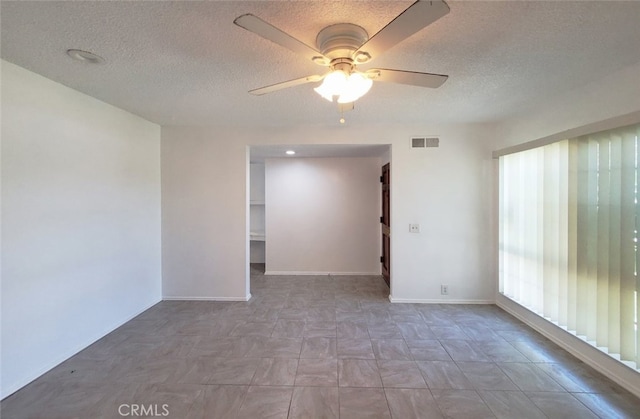 empty room featuring ceiling fan, baseboards, a textured ceiling, and visible vents