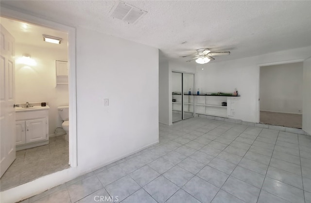 unfurnished living room featuring visible vents, a ceiling fan, light tile patterned floors, a sink, and a textured ceiling