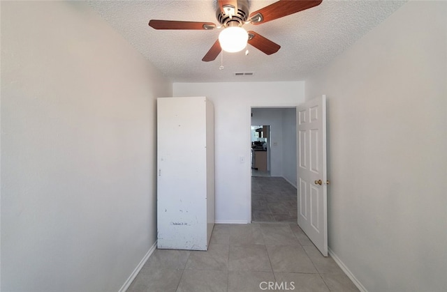 interior space featuring a textured ceiling, baseboards, visible vents, ceiling fan, and light tile patterned floors