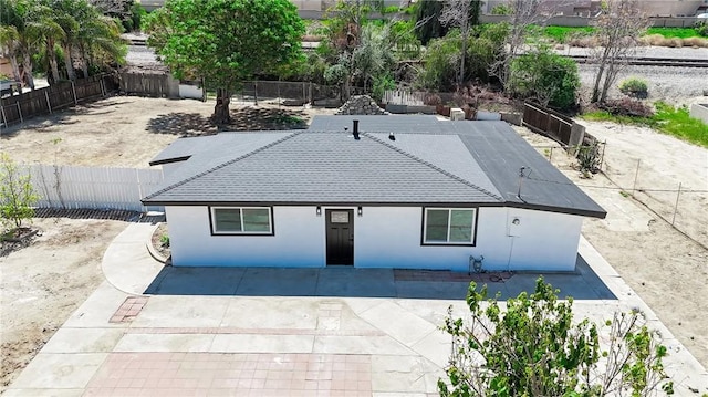 view of front of house with a patio, a shingled roof, a fenced backyard, and stucco siding