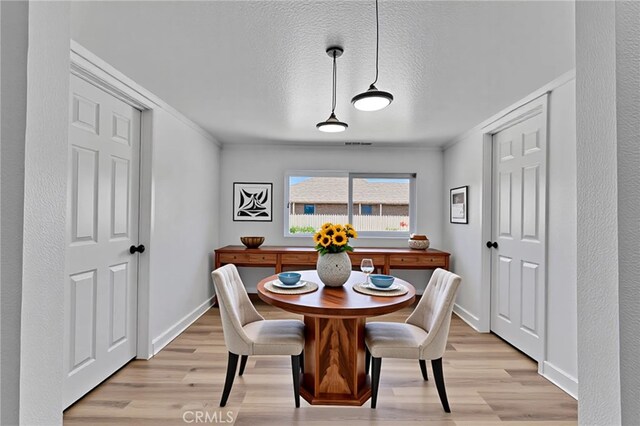 dining room featuring baseboards, light wood-style floors, visible vents, and crown molding