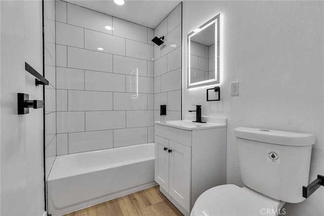 full bath featuring toilet, a textured wall, vanity, wood finished floors, and bathing tub / shower combination
