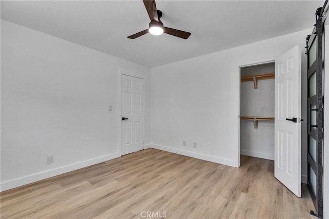unfurnished bedroom featuring a closet, baseboards, light wood-type flooring, and a barn door