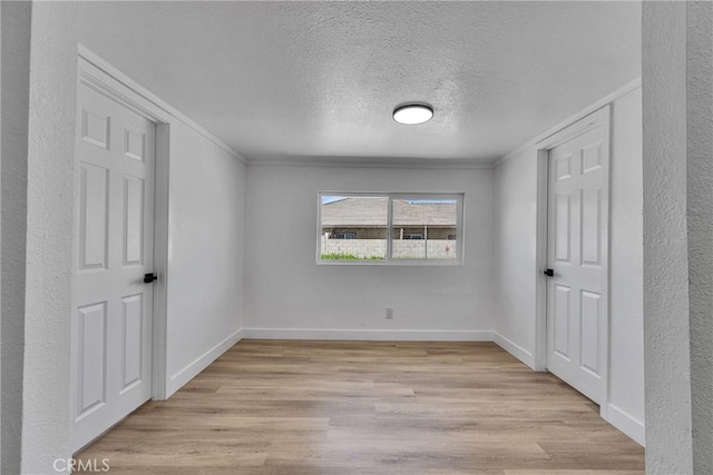 unfurnished bedroom featuring baseboards, light wood finished floors, a textured ceiling, and crown molding