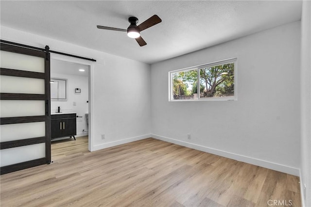 unfurnished bedroom with a barn door, baseboards, a ceiling fan, and light wood finished floors