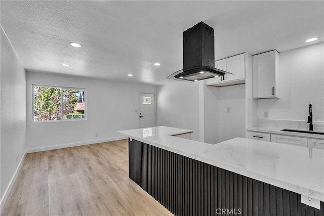 kitchen featuring a sink, white cabinets, light wood finished floors, and island exhaust hood
