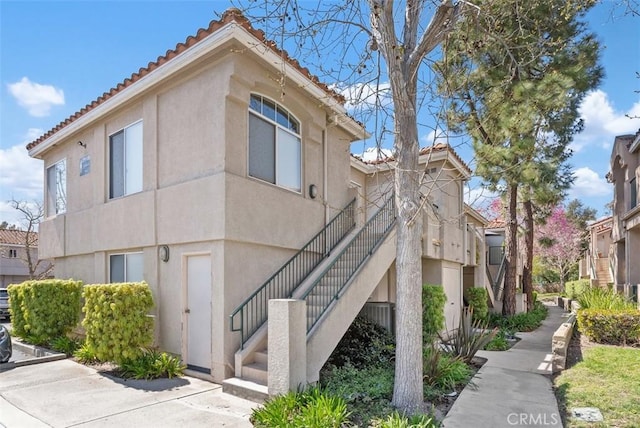 view of side of home featuring a tiled roof, stucco siding, and stairway