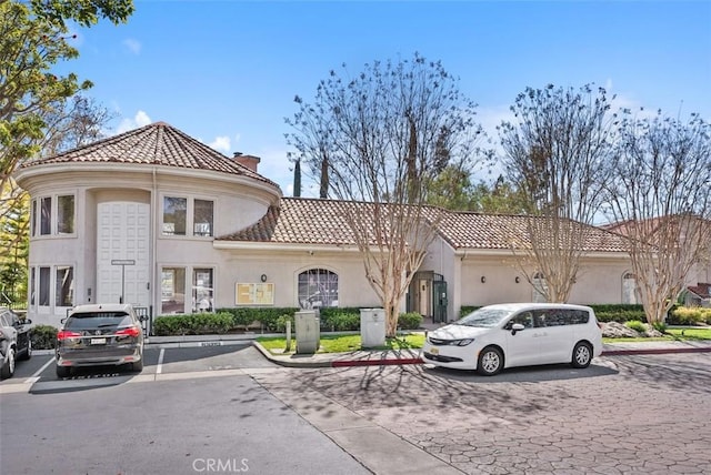 view of front of house with a tiled roof, a chimney, uncovered parking, and stucco siding