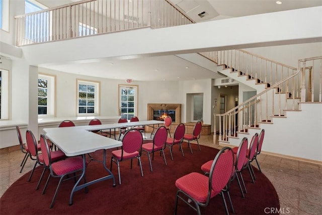 dining space featuring stairs, visible vents, a towering ceiling, a glass covered fireplace, and recessed lighting