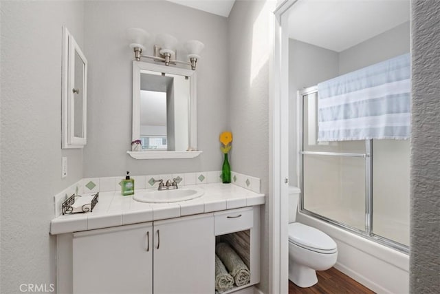 bathroom with vanity, toilet, bath / shower combo with glass door, and wood finished floors