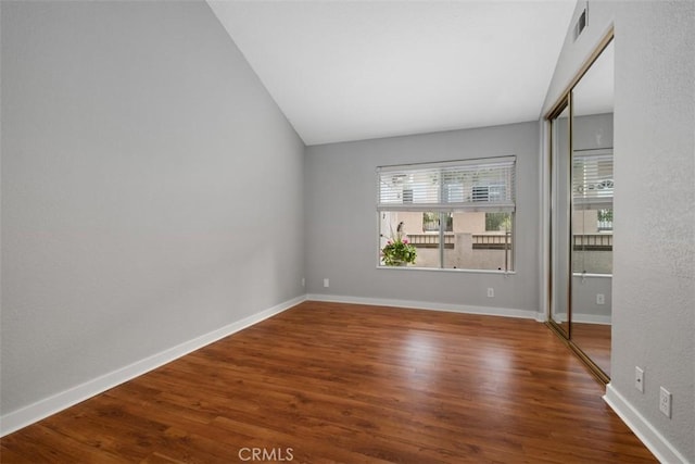 empty room with visible vents, baseboards, wood finished floors, and vaulted ceiling