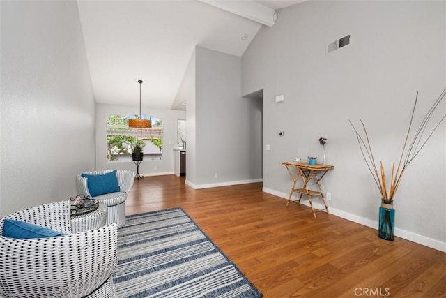 sitting room featuring wood finished floors, high vaulted ceiling, visible vents, baseboards, and beamed ceiling