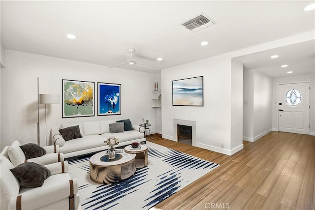 living room featuring baseboards, recessed lighting, a fireplace, visible vents, and light wood finished floors