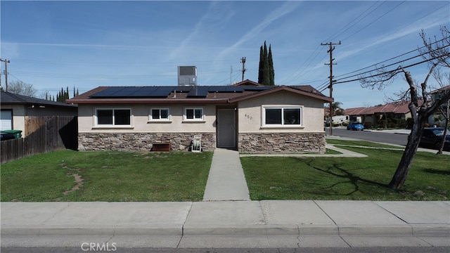 view of front of property with stone siding, fence, a front yard, solar panels, and stucco siding
