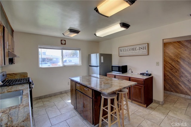 kitchen with a kitchen bar, under cabinet range hood, a kitchen island, a sink, and appliances with stainless steel finishes