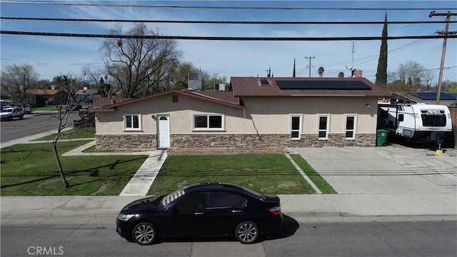view of front facade with stone siding, central air condition unit, roof mounted solar panels, a front yard, and stucco siding