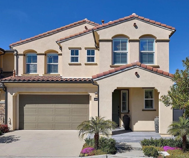 mediterranean / spanish house with a garage, stucco siding, a tiled roof, and concrete driveway
