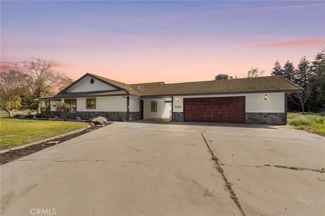 ranch-style home with a tile roof, a yard, concrete driveway, an attached garage, and stone siding