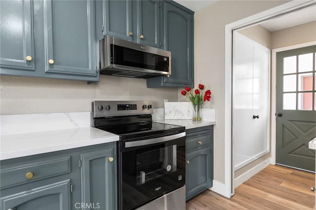 kitchen with blue cabinetry, light stone countertops, baseboards, light wood finished floors, and stainless steel appliances