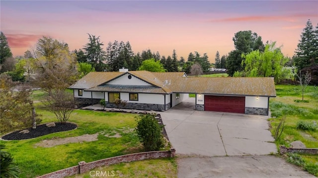 5703 Violet Ct, Atwater, CA 95301 - ranch-style home with stone siding, a garage, concrete driveway, a front lawn, and view of wooded area