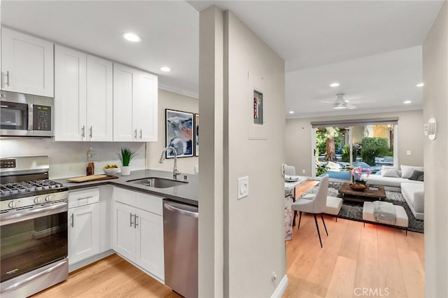 kitchen with light wood finished floors, white cabinets, a sink, open floor plan, and appliances with stainless steel finishes