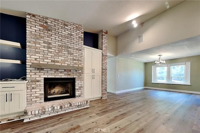 2100 Sherwood Ave Unit A, Modesto, CA 95350 - unfurnished living room with a brick fireplace, a notable chandelier, light wood-style flooring, and a textured ceiling