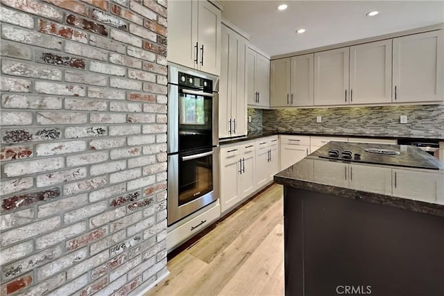 2100 Sherwood Ave Unit A, Modesto, CA 95350 - kitchen featuring stainless steel double oven, black electric stovetop, light wood-style floors, decorative backsplash, and dark stone counters