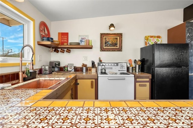 kitchen featuring freestanding refrigerator, white range with electric cooktop, open shelves, a sink, and tile patterned floors