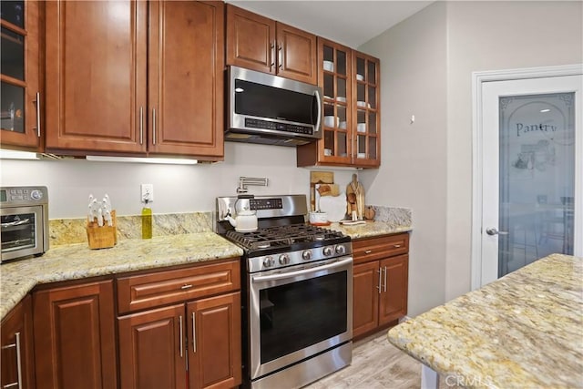 13083 Via Tuscany, Riverside, CA 92503 - kitchen with stainless steel appliances, light wood-style flooring, glass insert cabinets, light stone counters, and brown cabinetry