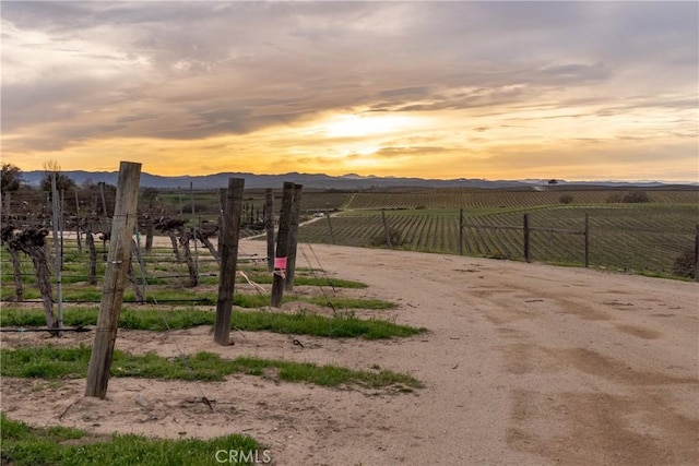 yard at dusk with a mountain view, fence, and a rural view