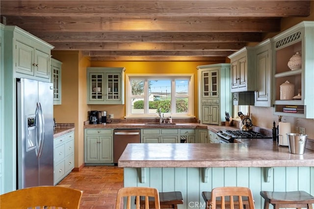 kitchen with green cabinets, a sink, stainless steel appliances, and a peninsula