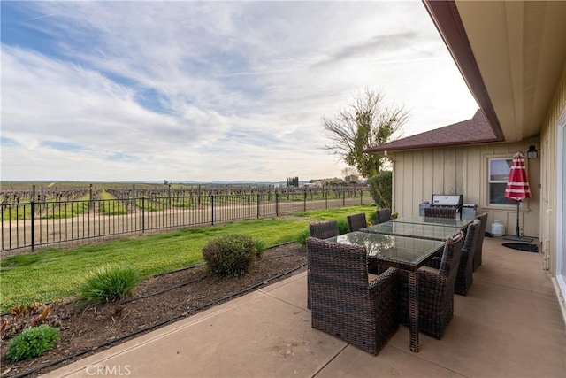 view of patio with a rural view, outdoor dining area, and fence