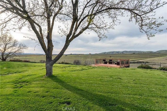 view of yard with a deck, fence, and a rural view