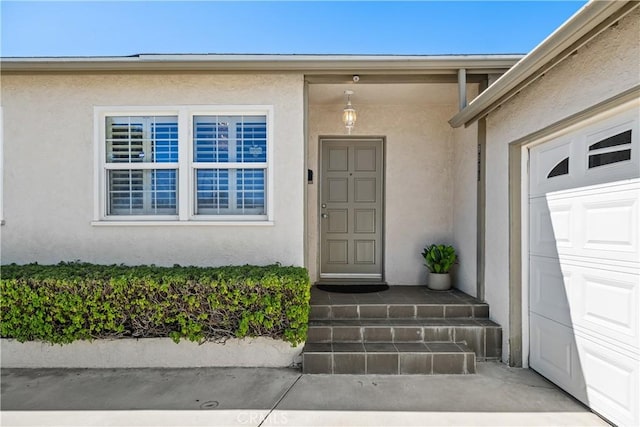 view of exterior entry with stucco siding and an attached garage