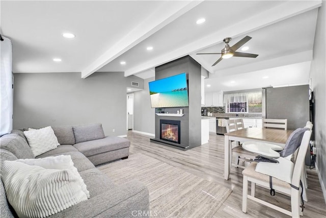 living area featuring vaulted ceiling with beams, a large fireplace, light wood-type flooring, ceiling fan, and recessed lighting