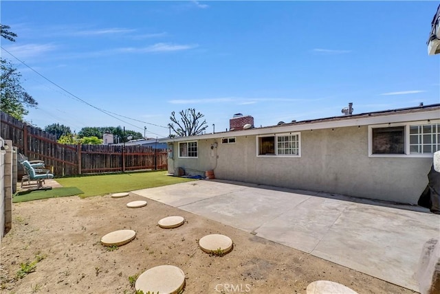 back of property with a patio, a chimney, a fenced backyard, stucco siding, and a lawn