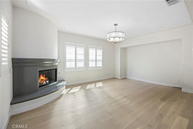 68 Sanctuary, Irvine, CA 92620 - unfurnished living room featuring a chandelier, a glass covered fireplace, light wood-style flooring, and baseboards