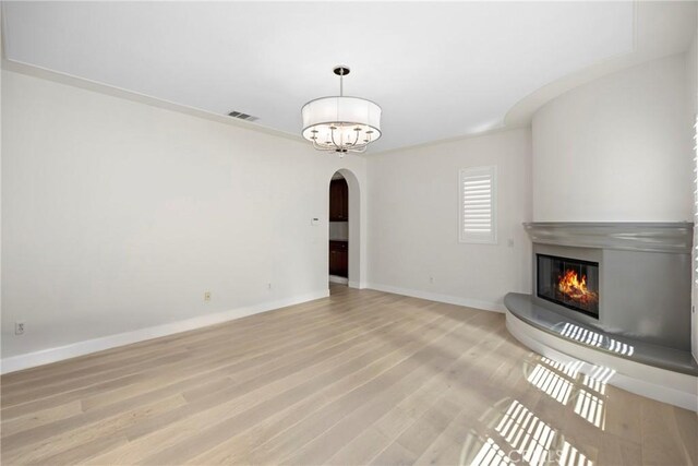 68 Sanctuary, Irvine, CA 92620 - unfurnished living room featuring arched walkways, a glass covered fireplace, light wood finished floors, and baseboards