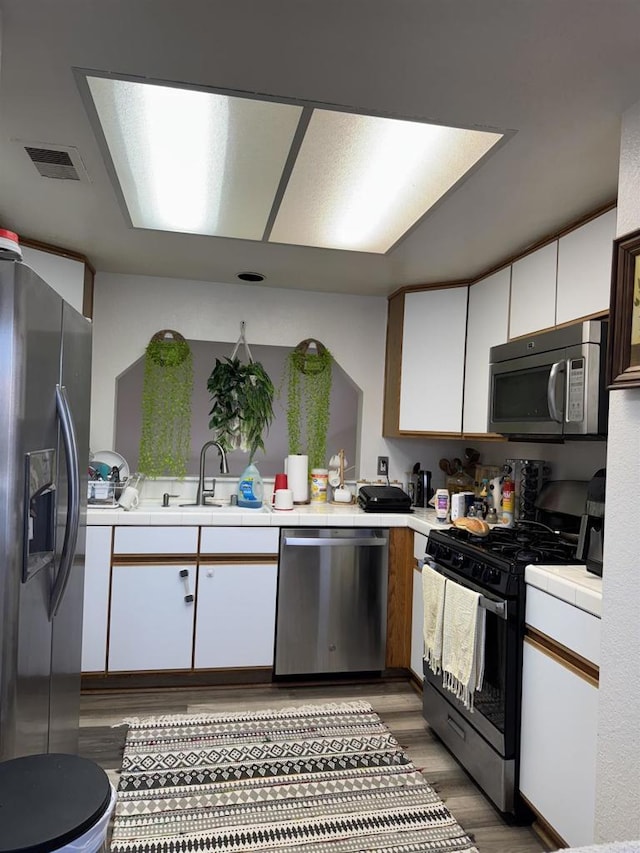 12090 Calle De Montana Unit 251, El Cajon, CA 92019 - kitchen with tile counters, light wood-style flooring, stainless steel appliances, visible vents, and white cabinets