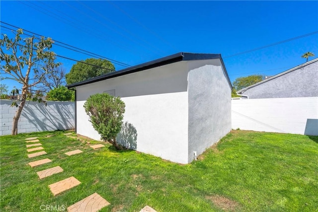 view of side of property featuring stucco siding, an outbuilding, fence, and a yard