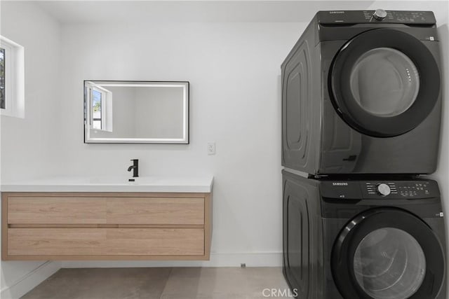 laundry area featuring stacked washer / dryer, a sink, baseboards, and laundry area