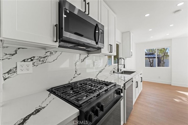 kitchen with tasteful backsplash, light wood-type flooring, stainless steel appliances, a sink, and white cabinets