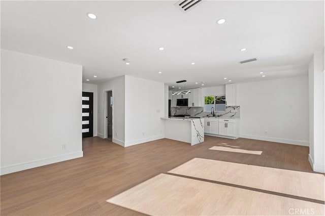 unfurnished living room featuring a sink, visible vents, light wood-style floors, and recessed lighting