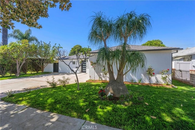 view of front of property featuring a front yard, driveway, stucco siding, and fence