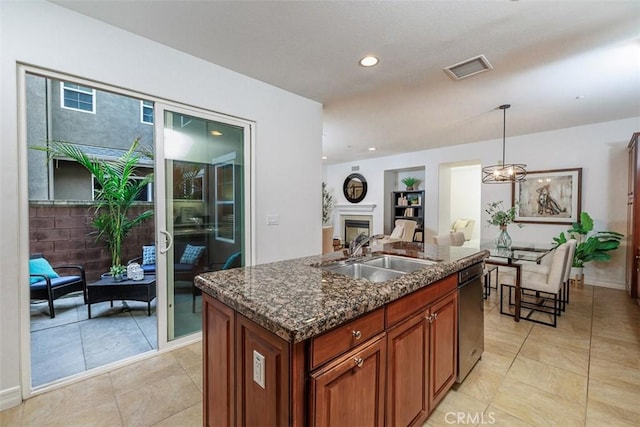 kitchen with a sink, a fireplace, dark stone counters, decorative light fixtures, and open floor plan