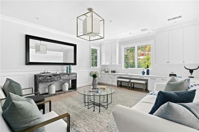 living room with wainscoting, ornamental molding, light wood-style flooring, and visible vents