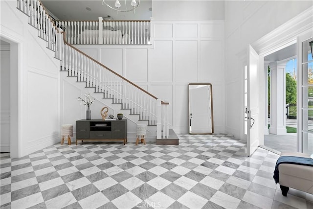 foyer entrance with stairs, a towering ceiling, a decorative wall, and an inviting chandelier
