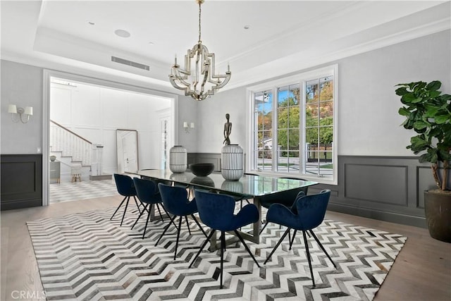 dining space with crown molding, stairway, a decorative wall, and a raised ceiling
